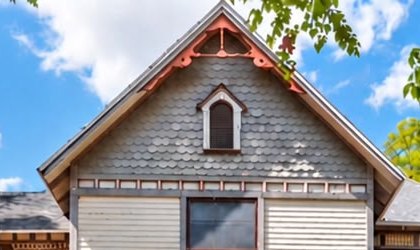 The front gable with grey fish-scale shingles and an arched attic window.