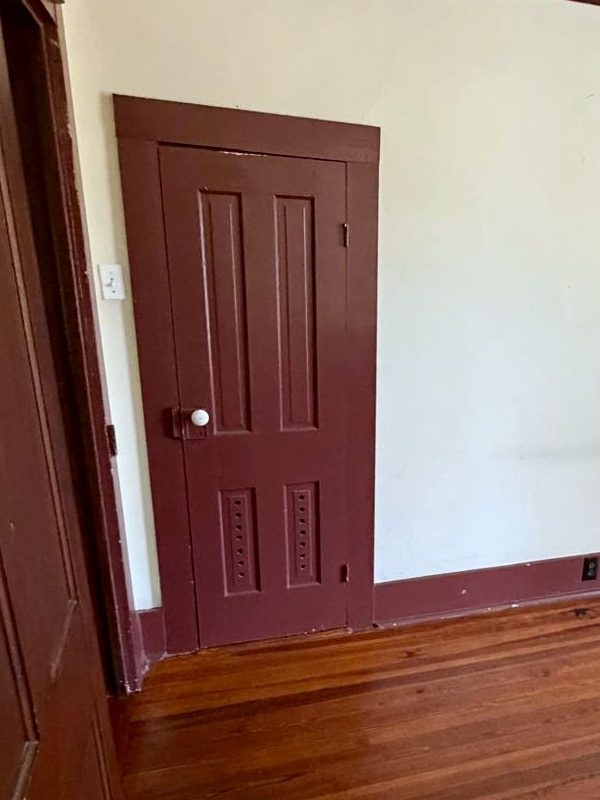 A dark red four-panel closet door with pierced Eastlake panels and a white porcelain knob.