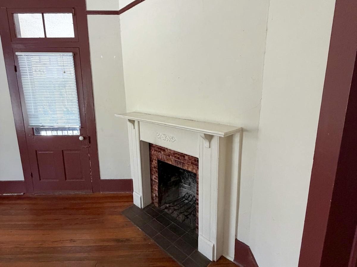 A white painted mantel with a brick-tiled fireplace and slate hearth, beside a paneled door with a transom window.